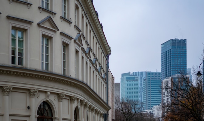 Historic Townhouse Facade With Columns In Foreground Contrasted By Modern Warsaw Skyscrapers Under Overcast Urban Sky
